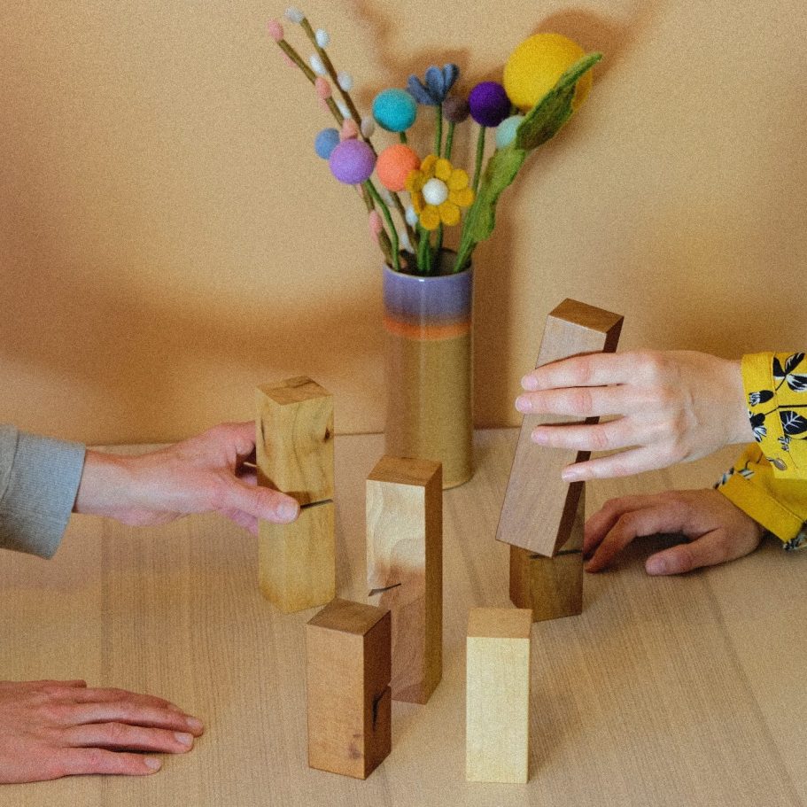 Zwei Hände stellen ein System mit Holzklötze auf dem Tisch im Beratungsraum.